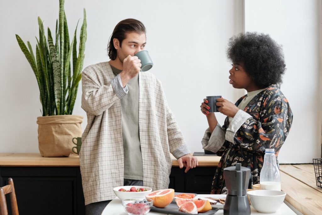 Interracial couple of White man and African American woman, talking in kitchen while having breakfast.