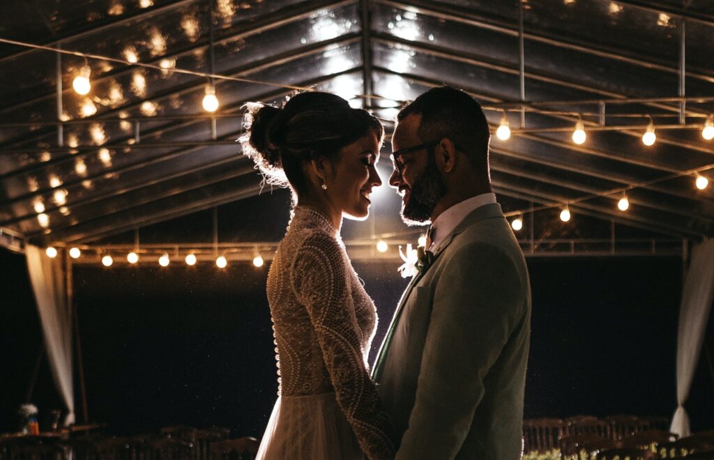 Groom standing closely facing his bride in dark room lit with twinkle lights