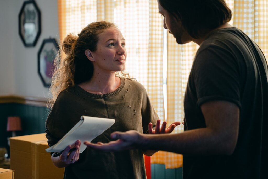 Curly red headed White woman holding notepad, trying to apologize to male partner