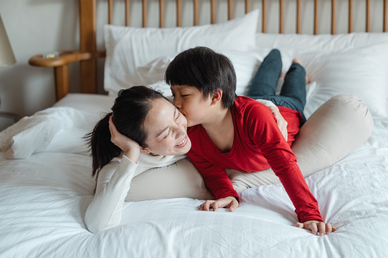 Cheerful Asian mom and son playing on top of bed