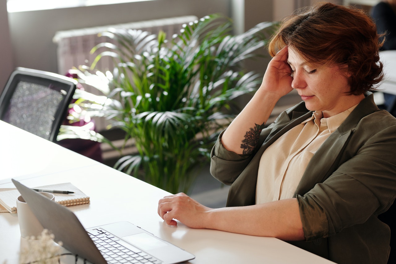 Middle aged red hair White woman sitting with right hand to temple, experiencing burnout.