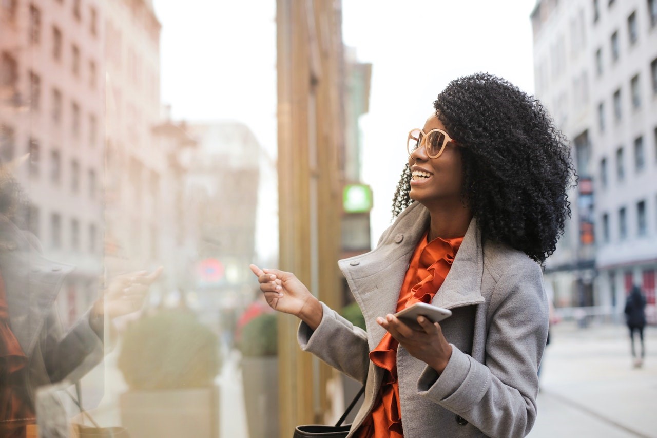 Black woman standing downtown wearing grey peacoat over orange blouse, full of gratitude.