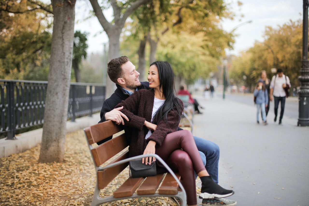 Asian woman sitting on a white man on a bench in a park in a happy marriage.