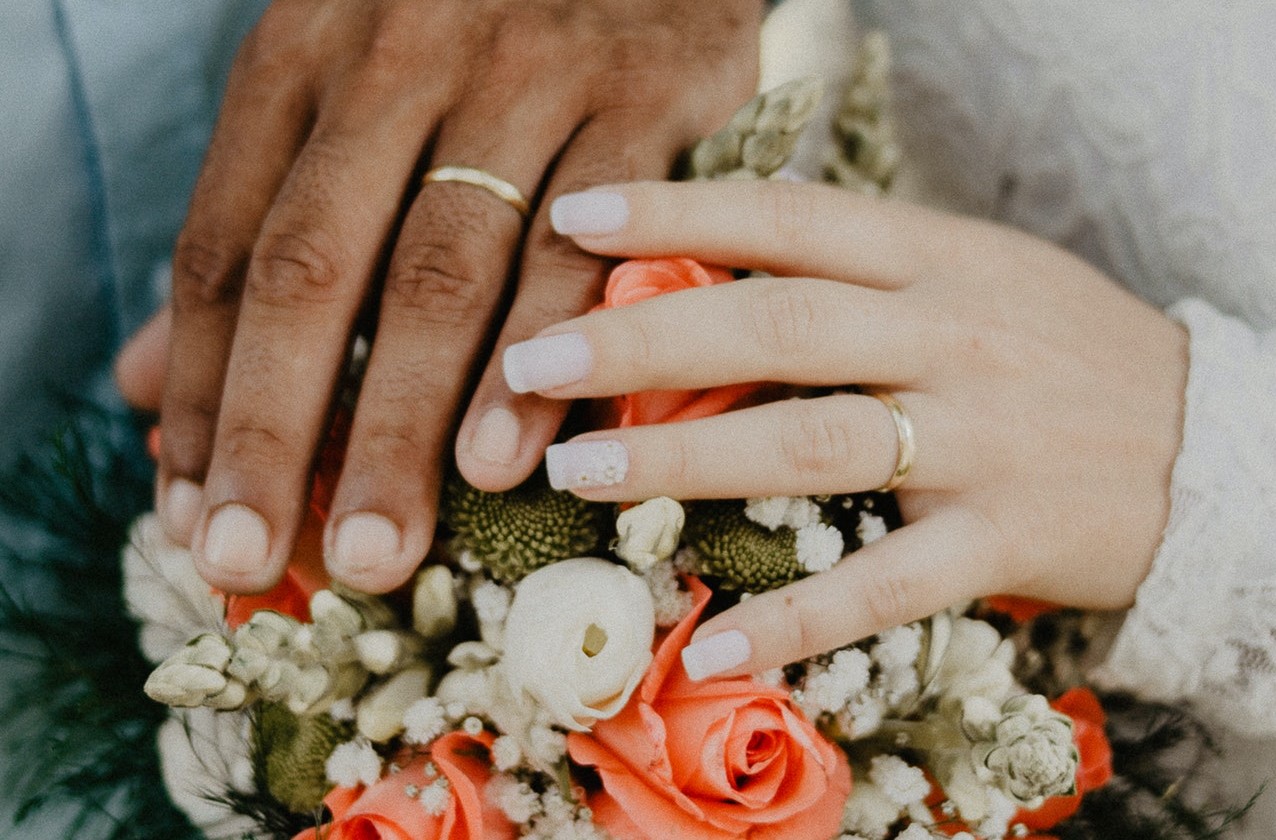 Hands of male and female couple over wedding bouquet with their marriage rings.