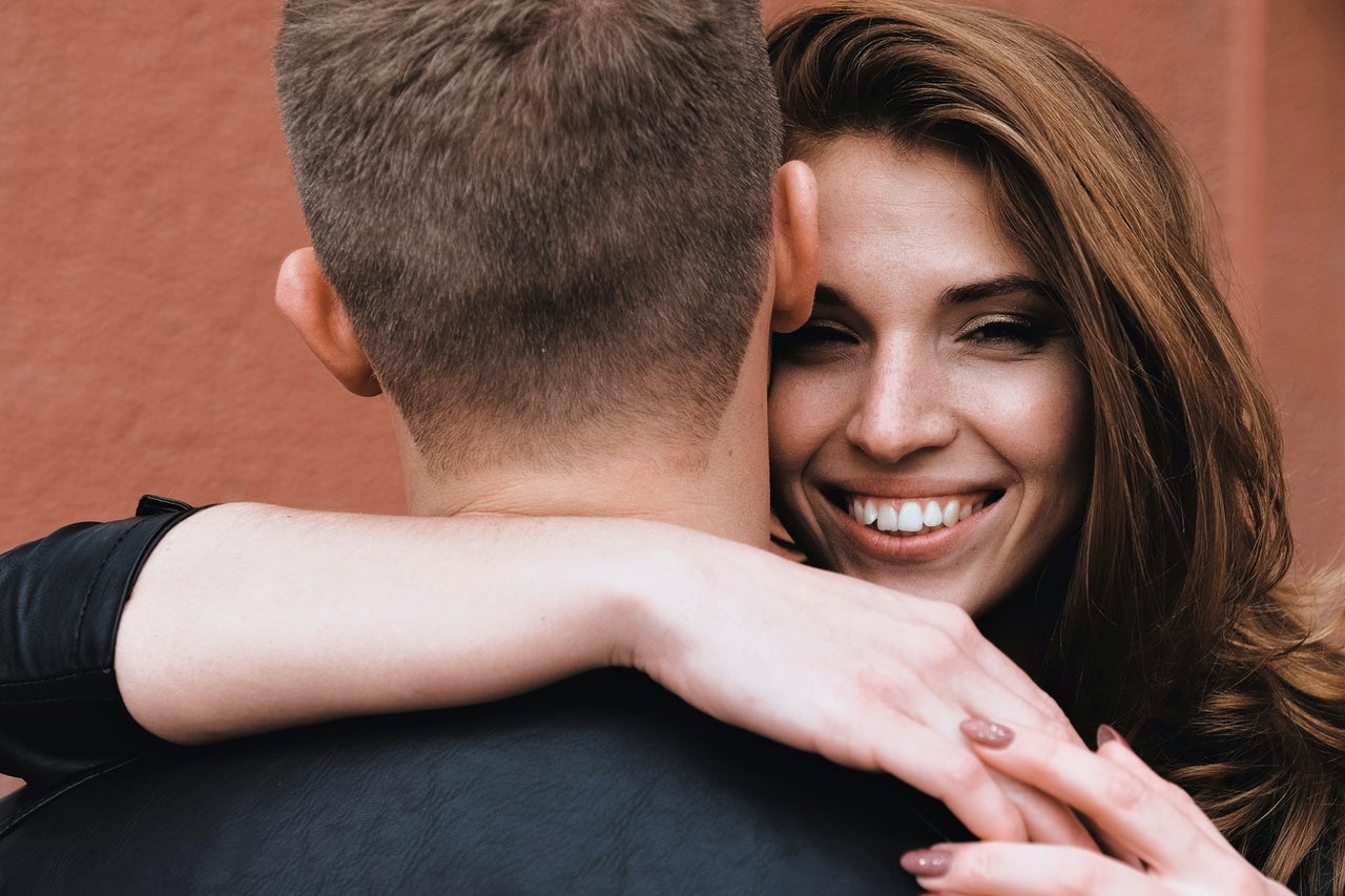 White woman expressing her love languages, physical touch, by wrapping her arms around the neck of a man.