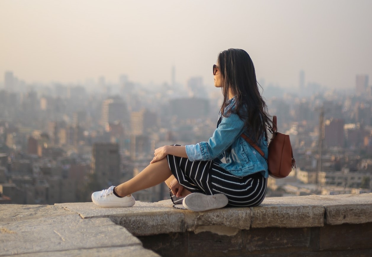 Asian woman sitting on ledge of building contemplating what is her value.