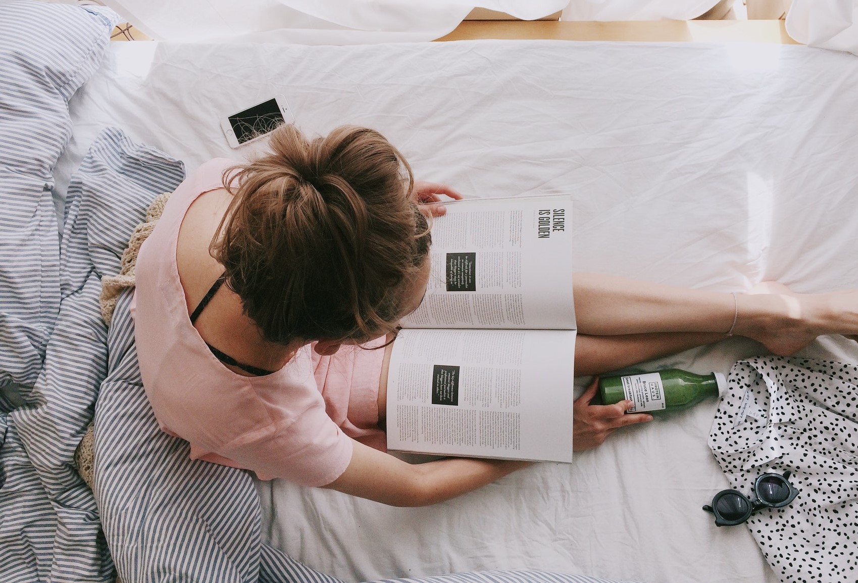 Young white woman sitting on her bed reading about identity.