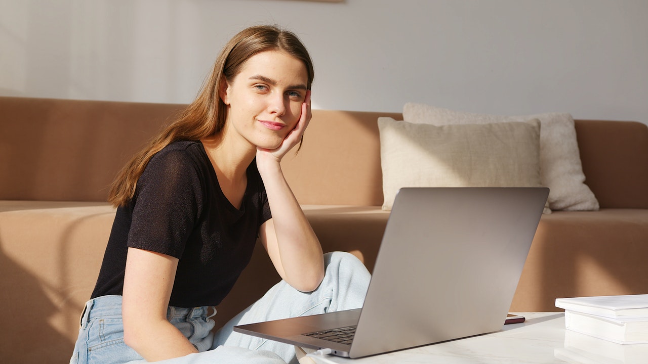 Young White woman sitting on her bed with a laptop procrastinating.