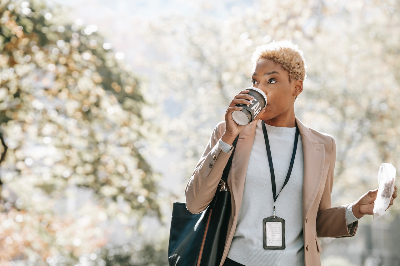 Young African American businesswoman drinking takeaway beverage during coffee break in park practicing time management.